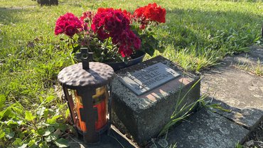 Das Bild zeigt einen Grabstein auf der Kriegsgräberstätte Butzbach Nieder-Weisel. Neben dem GRabstein steht eine Grabkerze, hinter dem GRabstein ist eine GRabschale mit Blumen zu sehen.