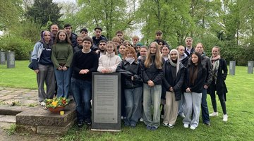 Ein Gruppe von Schülerinnen und Schülern steht hinter einer Informationstafel auf dem Friedhof Kassel-Bettenhausen.